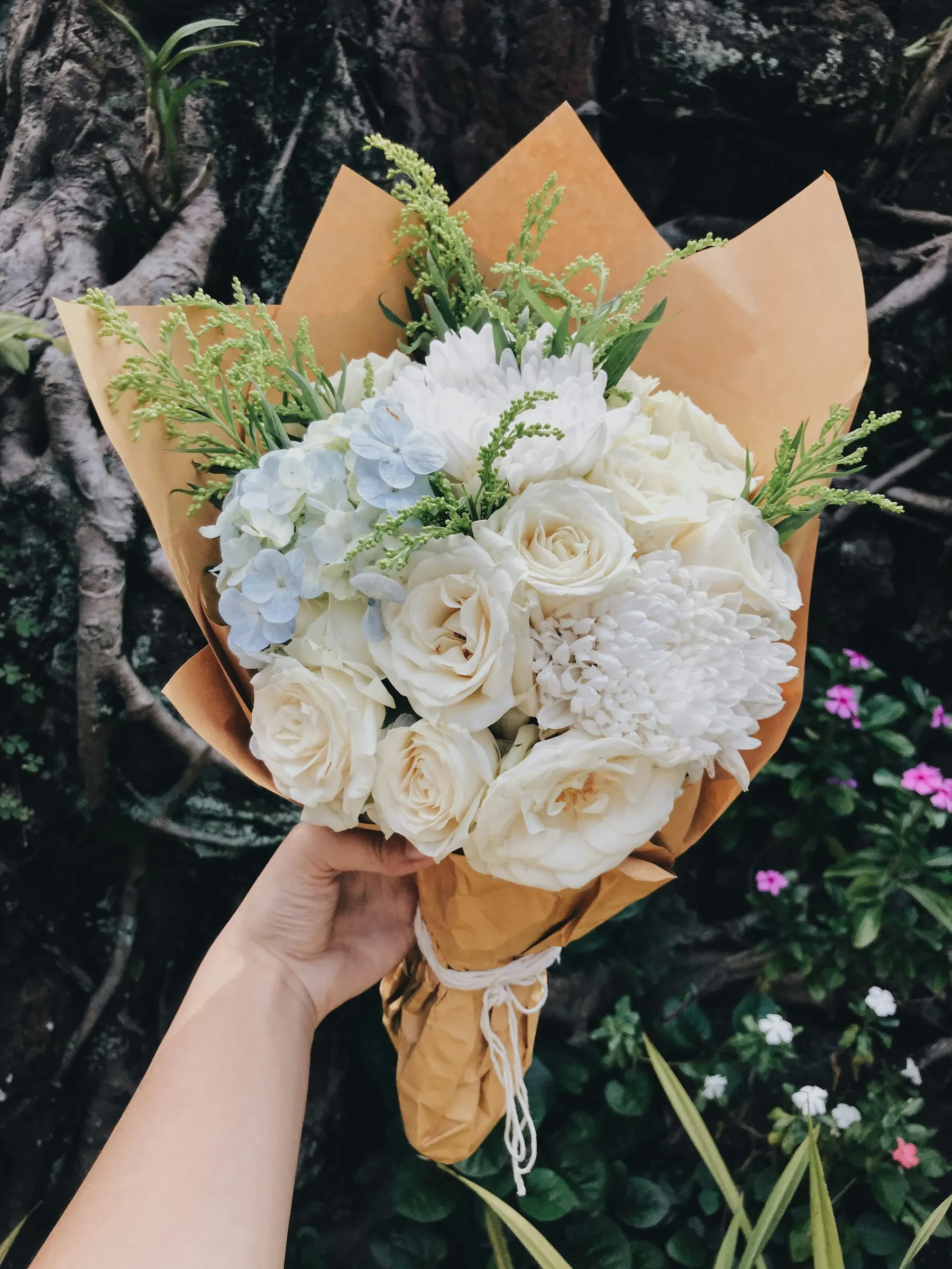 Eine Hand hält einen in Packpapier gewickelten Strauß aus weißen Rosen